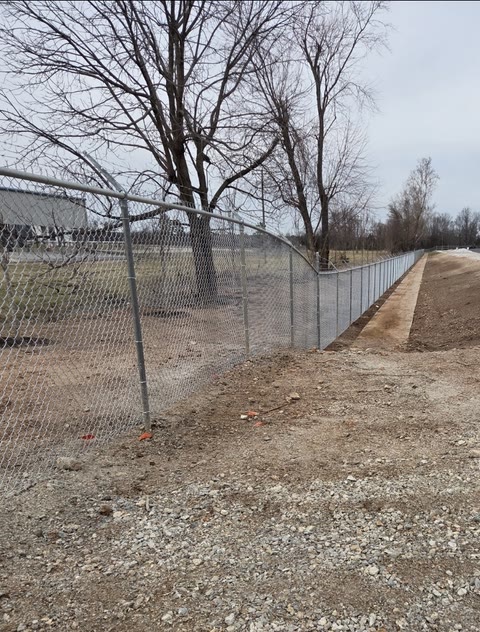Galvanized chain-link fence running along a graded commercial lot in Northwest Arkansas