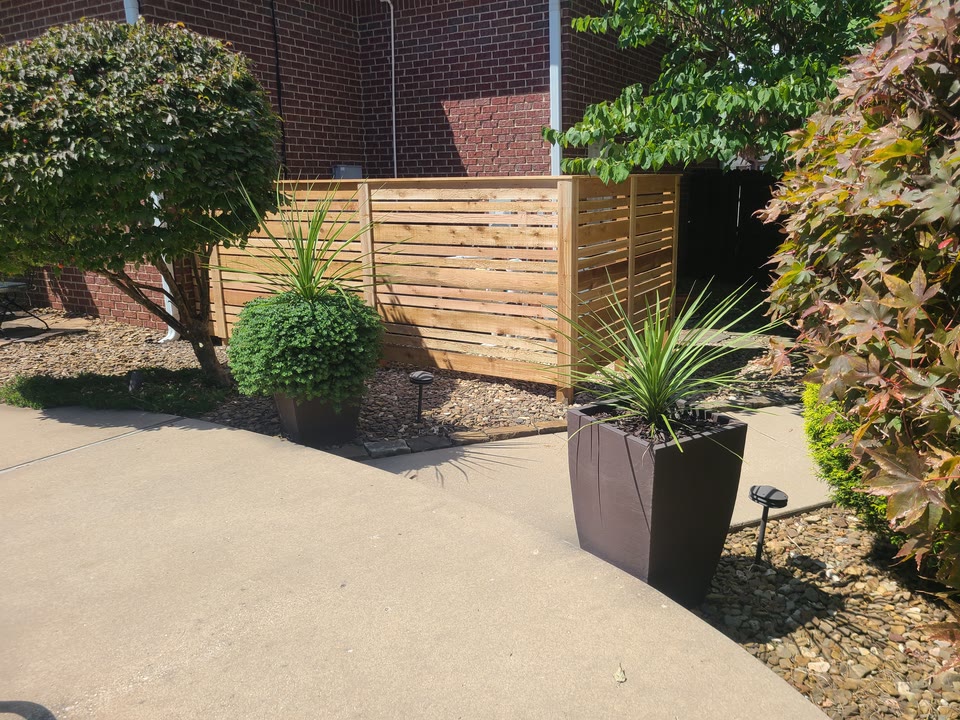 Custom cedar-slat screen enclosing pool equipment beside a brick building in Northwest Arkansas