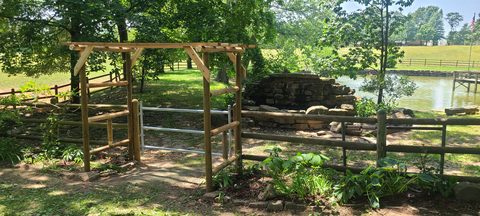 Custom cedar arbor and split-rail fence beside a private pond in Northwest Arkansas