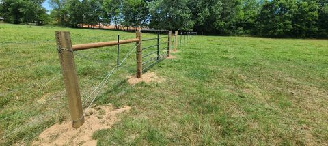 Pipe-and-cable ranch fence with round wood posts along a pasture in Northwest Arkansas